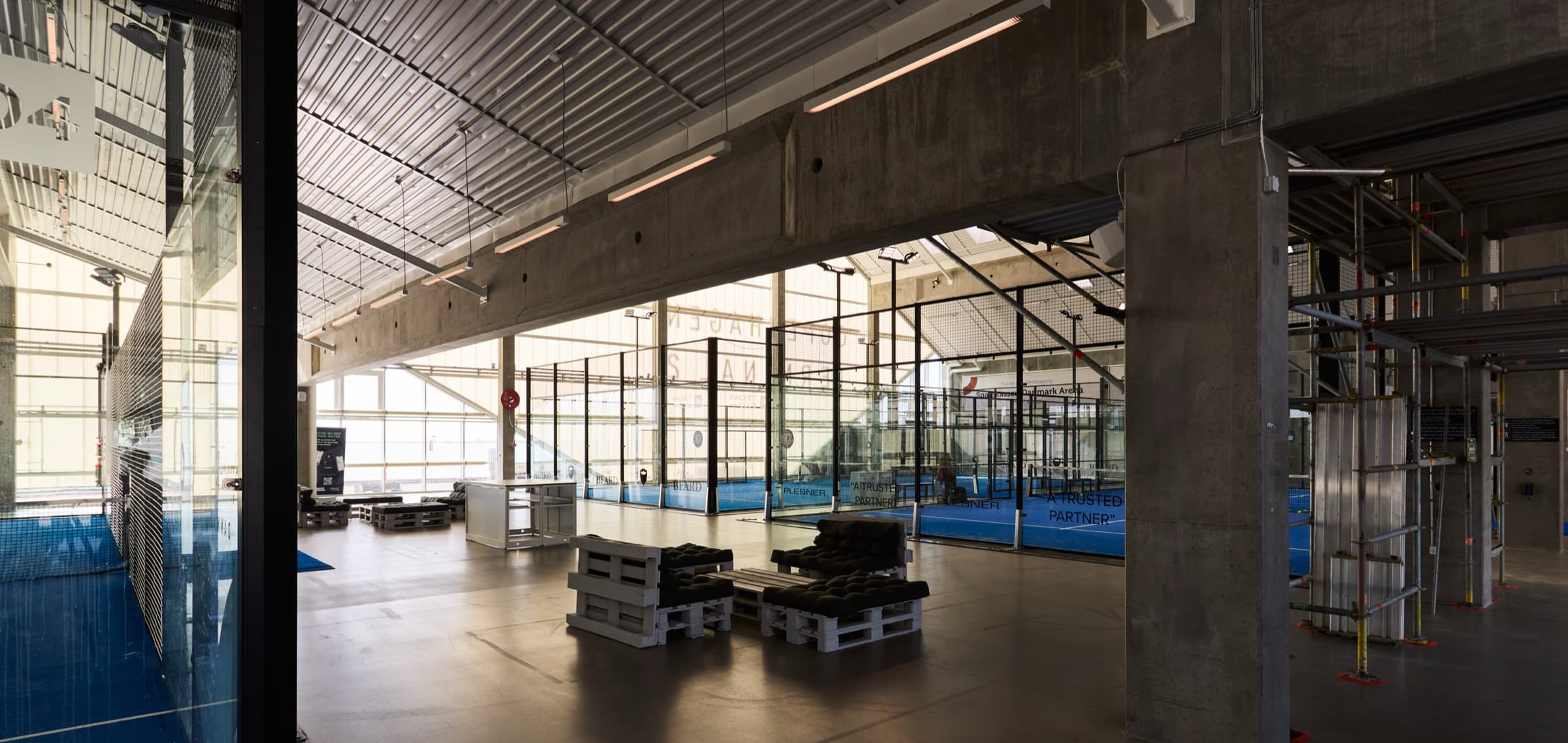 Indendørs padelhal hos Racket Club med rå betonsøjler, ståltag og baner bag glas